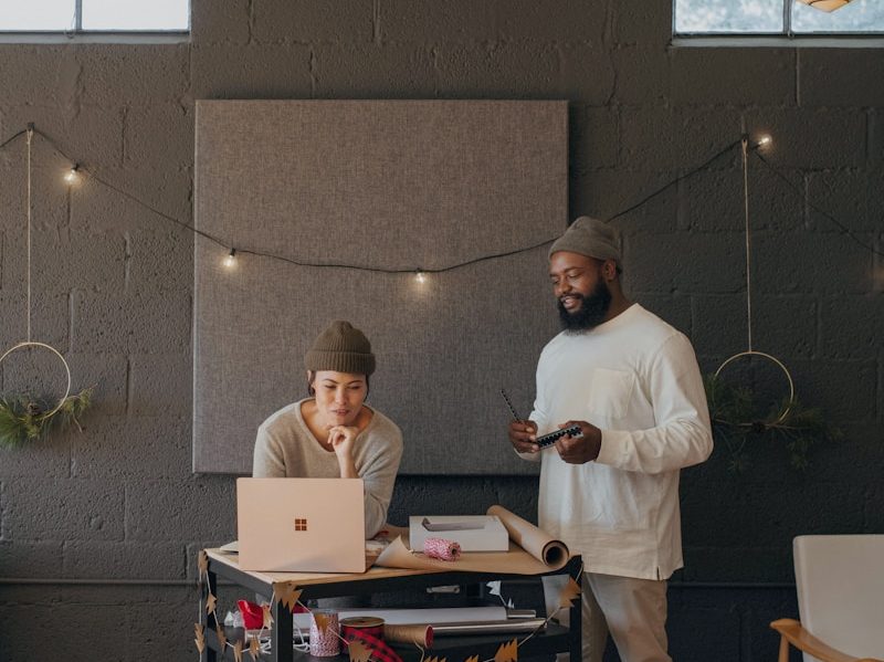 Two coworkers on a Surface laptop with Christmas presents on a cart